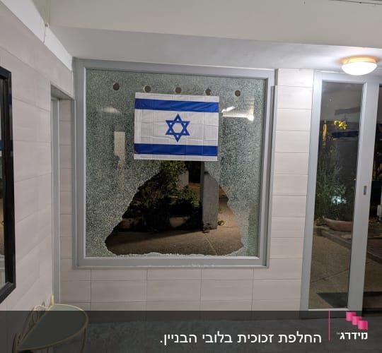 חלון שבור עם דגל ישראל תלוי עליו